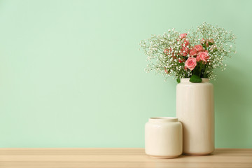 Stylish vase with beautiful bouquet on table near color wall