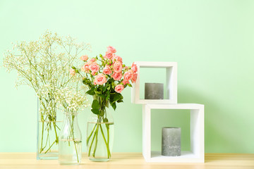 Stylish vases with beautiful flowers and candles on table near color wall