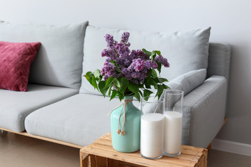 Beautiful lilac flowers on table and sofa in interior of room