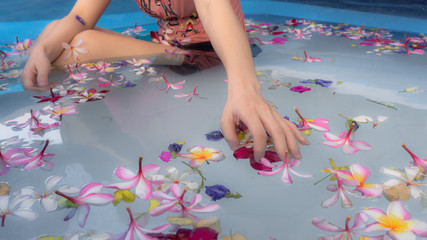 Fototapeta na wymiar A woman soaking in the water with flowers in swimming pool. taking care, spa and relaxation. taking holiday concept.