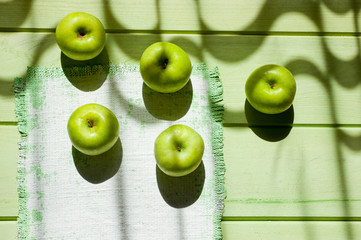 Fototapeta na wymiar Ripe green apples on a light green painted wooden surface, illuminated by sunlight from a window through curtains. Background for fruits. Black and white drawing with natural light.
