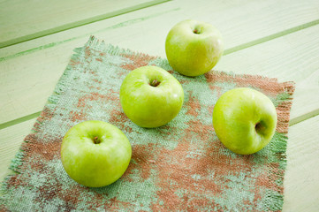 Ripe green apples on a green napkin lying on a canvas napkin and a wooden table surface. Background for fruits.