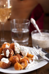 Round fried mozzarella cheese sticks under creamy sauce, glass of wine and water on wooden rustic background.