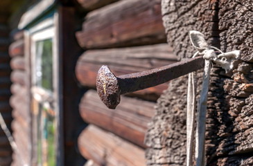Vintage metal forged nail closeup against a log wall with a window of an old house