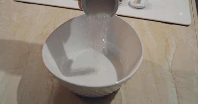 Pouring of two tablespoon of sugar in a bowl on a kitchen countertop
