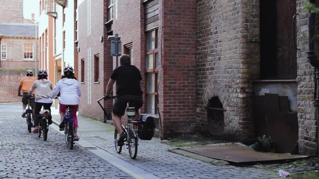 A group of adults cycling down a cobblestone road in England, UK.