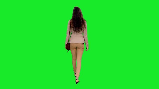 Back view of young stylish woman with shoulder bag walking and stumbling on green screen background, Chroma key