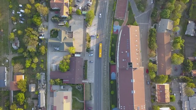 Yellow bus driving on urban road curve, overhead aerial tracking drone