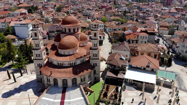 Cathedral with high bell towers and red roofs in city center surrounded by big square and traditional houses in Korca, Albania