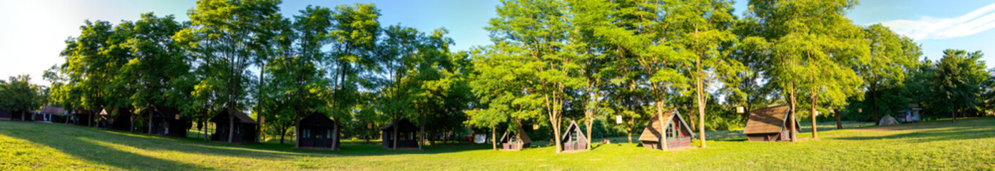 panorama with camping with wooden chalets and green grass and trees