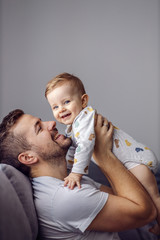 Young attractive caring father holding his beloved little son, singing song to him and having fun.