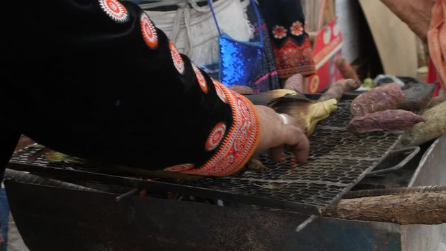 Tribal lifestyle. Hmong people are grilling sweetcorn and purple sweet potato with bare hands. Glowing flame on the corns. Hmong people are in their beautiful traditional tribal dress.