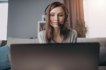 lose up of attractive woman wearing headset while working on personal laptop at home. Young girl...
