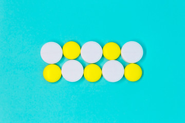 white and yellow round pills in a row on a blue background close-up layout. medical treatment copy space concept 