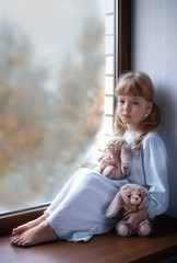 
bored blond girl sitting by the window with her toy