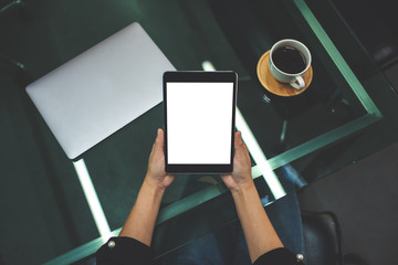 Top view mockup image of businesswoman holding black tablet pc with blank white screen in the office , laptop and coffee cup on the table