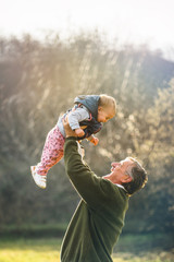Grandfather proudly rising his granddaugther above his head while enjoying sunny day outdoors.