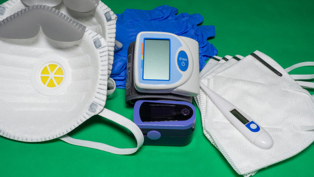 Medical Kit: Digital Body Thermometer, Pulse Oximeter, Medical Mask And Arm Blood Pressure Monitor. Disposable Medical Gloves. Kit To Check Values During Coronavirus Covid 19. Green Background