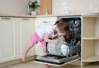 Open dishwasher with dirty dishes. Little girl helps to lay the dishes. Mom's little helper. Kitchen