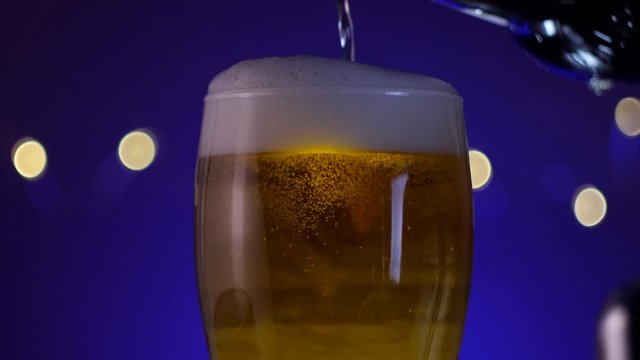 Pouring beer to the glass wwith bubbles and foam on blue background