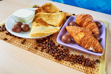 Croissants, pancakes, chocolates with milk and kefir are on the mat. Continental breakfast