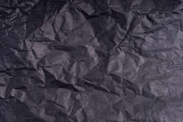 Dark wrinkled creased black paper poster texture. Blank creased crumpled grainy paper textured surface.