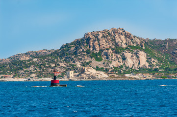 A view of a buoy for nautical signaling in the blue sea on a sunny day with in the background the coast of the island and its houses, in Sardinia Italy