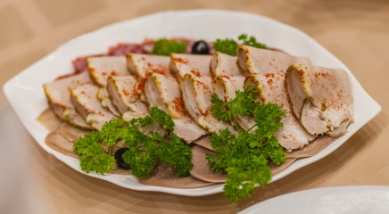 Sliced boiled meat and sprigs of parsley close up on a white plate on a tablecloth background