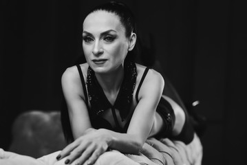 Naklejka premium A portrait of a sexy girl model who lies on a bull of chic sofa. A slender girl in black fashion linen. looks in before. crossed hands. bw
