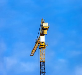 The top of the tower crane on the construction site against the blue sky with clouds