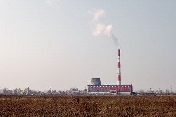 Fototapeta na wymiar A building of a thermal power plant with a smoking chimney and dry grasses on the foreground