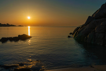A view of the sea from the coast with the sunrise sun reflecting off and brightening the rocks with the colors of a wonderful sunrise on a summer day, in Sardinia Italy