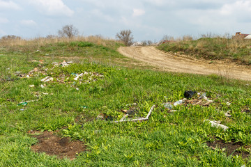 Household garbage is lying on a roadside of a rural unpaved road