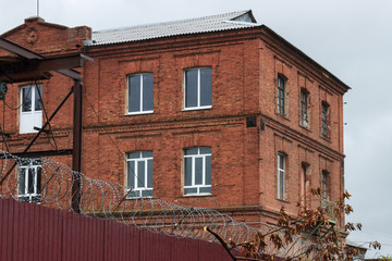 An old brick building behind a metal fence with barbed wire