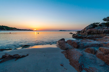 A view of a beach without people with the sun rising and brightening the rocks with dawn colors on a summer day holiday, in Sardinia Italy