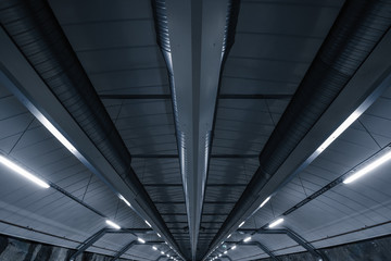 Sci fi looking dark and moody underground parking lot with fluorescent lights on.  Ceiling shot with ventilation tubes