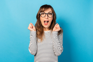 Portrait of a young friendly woman with a surprised face in a casual t-shirt and glasses on an isolated light background. Emotional face. Gesture of surprise, joy, shock