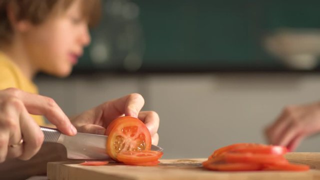 Children cooks pizza. Boy and girl having fun with father. Prepering ingredients for pizza. Slicing tomato