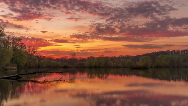 Time-lapse of moving clouds at sunset reflecting above the lake surface dark clouds of black and gray color moving in the sky the sun sets over the horizon Hustopece nad Becvou Czech Republic