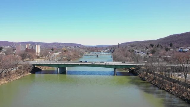 Drone flys over green river with bridge ahead with cars crossing in Binghamton New york
