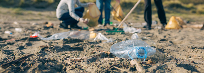 Group of senior volunteers picking up trash on the beach. Selective focus on plastic bottle in foreground