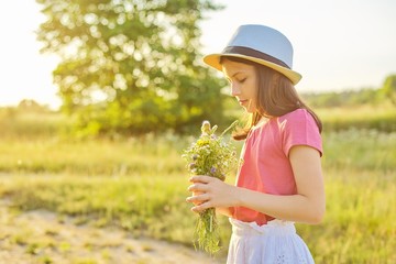 Beautiful girl child in hat, collecting bouquet of wildflowers in sunny meadow