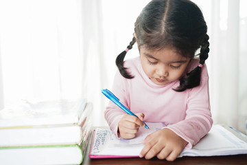 Asian student child girl writing on the paper book. Asian genius student doing a homework at home. education , study and learning concept.  