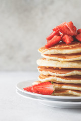 Pancakes with strawberries and honey on white plate.