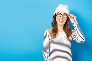 Portrait of a cute young woman in glasses, hat and sweater smiling on a blue background. Emotional face. Gesture of joy