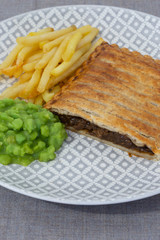 Steak and onion lattice pie with fries and mushy peas.  On a grey marl tablecloth