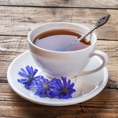 Cup with chicory drink and blue chicory flowers on wooden table. Copy space.