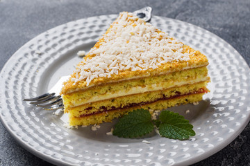 Piece of delicious puff cake with butter cream and berry jam on a plate with mint. Gray concrete background. Copy space.