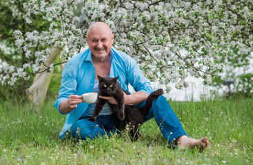 Naklejka na ściany i meble Portrait of Happy Mature man with a black cat at nature. Concept of senior lifestyle