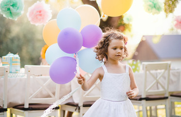 Portrait of small girl playing with balloons outdoors on garden party in summer.